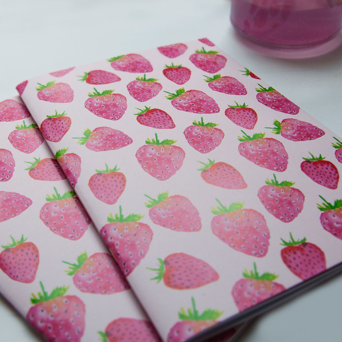 Two notebooks with strawberry pattern on a white surface