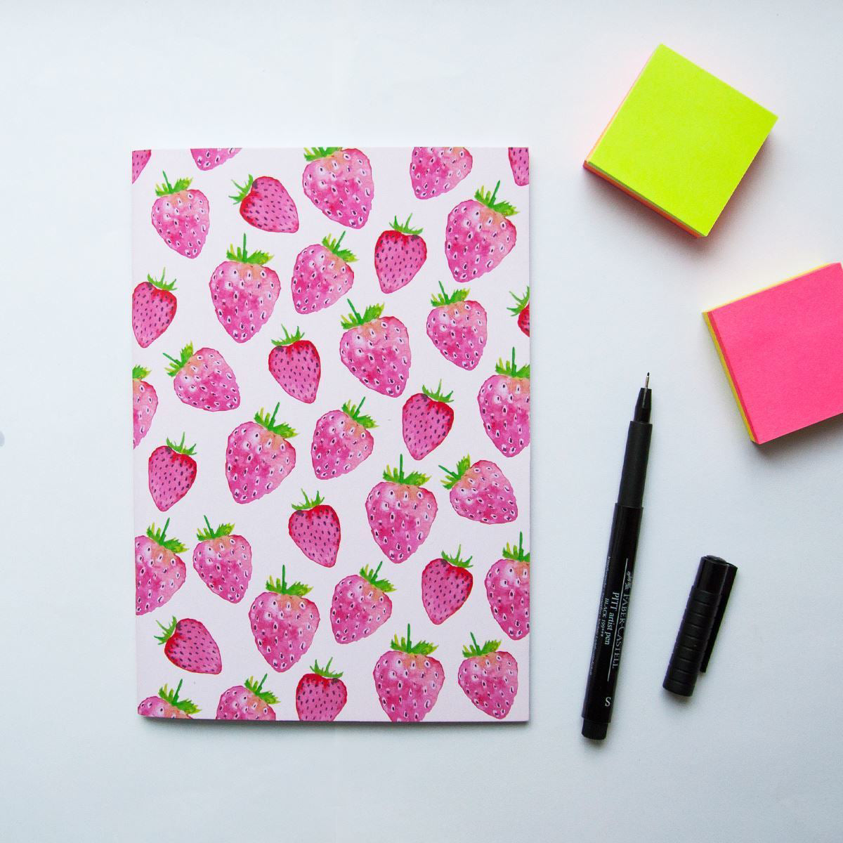 Notebook with strawberry pattern, pens, and sticky notes on a white background