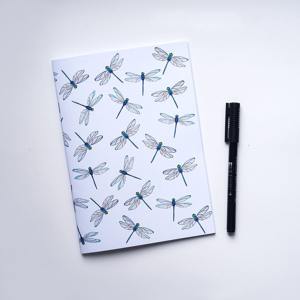 Notebook with dragonfly pattern and a pen on a white background