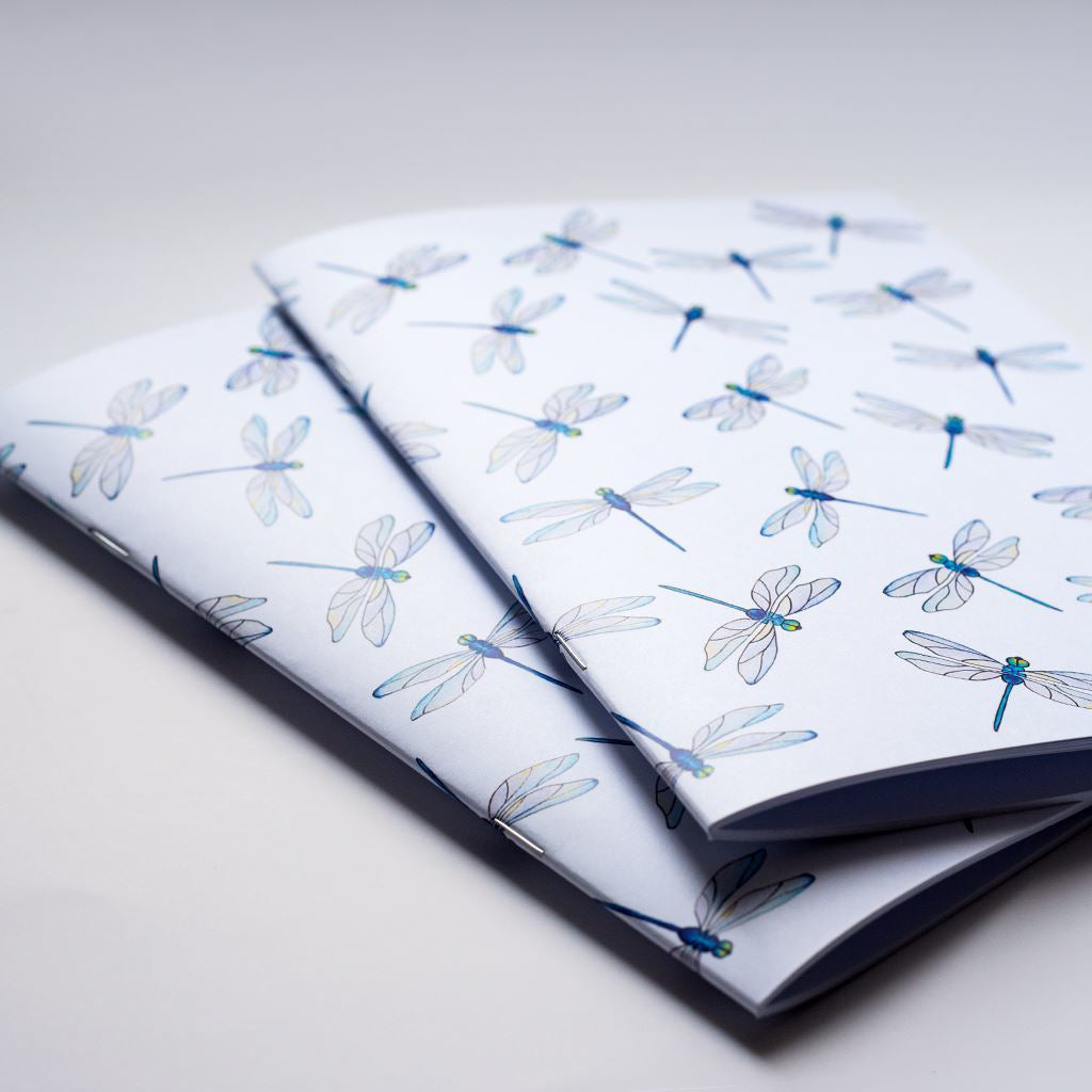 Two closed notebooks with dragonfly patterns on a light gray background