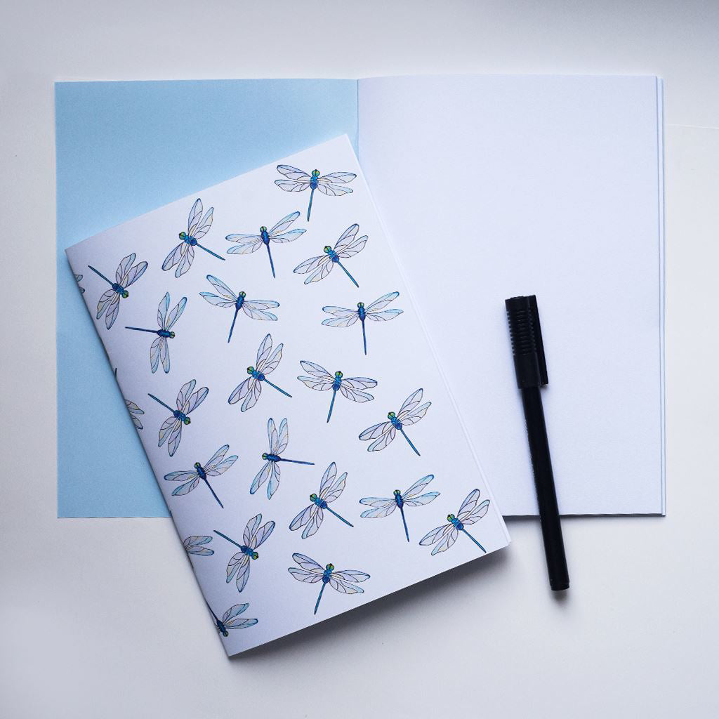 Notebook with dragonfly pattern on a light blue cover, with a pen on a white background