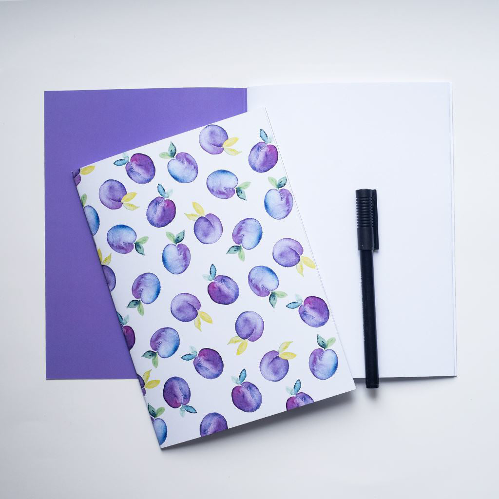 Notebook with purple plum pattern on top of an open notebook with a purple page