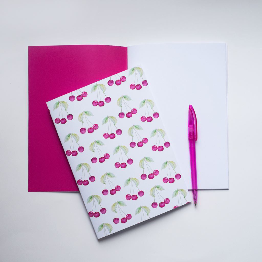 Notebook with cherry pattern, pink cover, and pink pen on a white background
