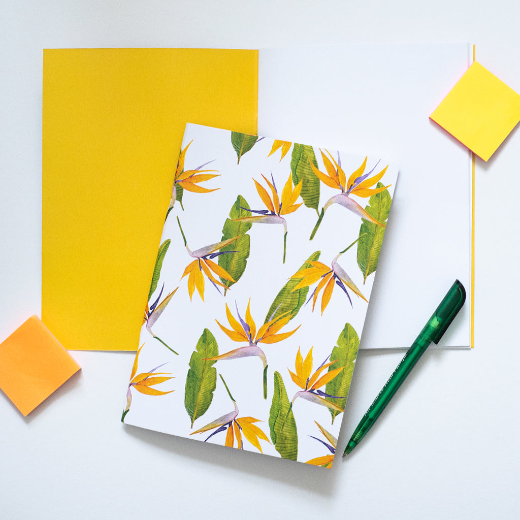 Notebook with tropical flower design, green pen, and yellow post-it notes on a white background