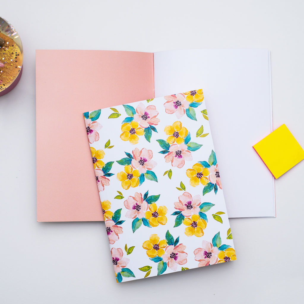 Floral notebook on a white surface with a pink cover and yellow sticky notes.