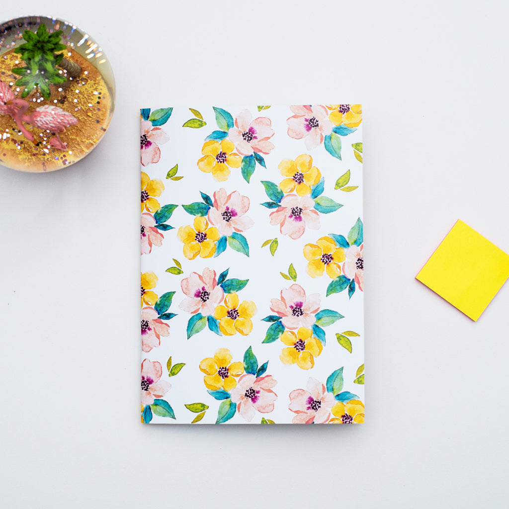 Floral-patterned notebook on a light gray surface with a yellow sticky note and decorative snow globe