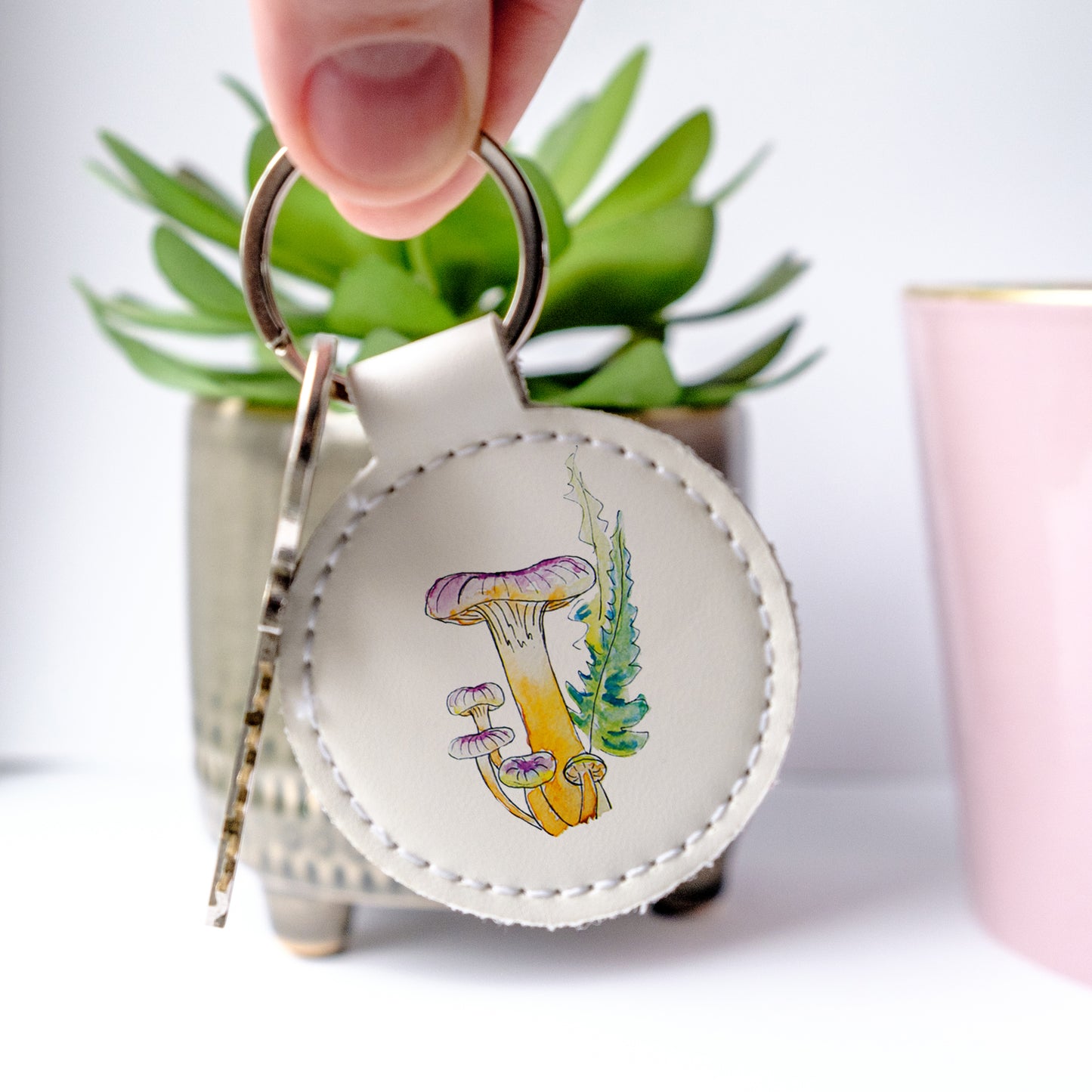 Round faux leather keychain with mushroom design held by a hand against a light background.