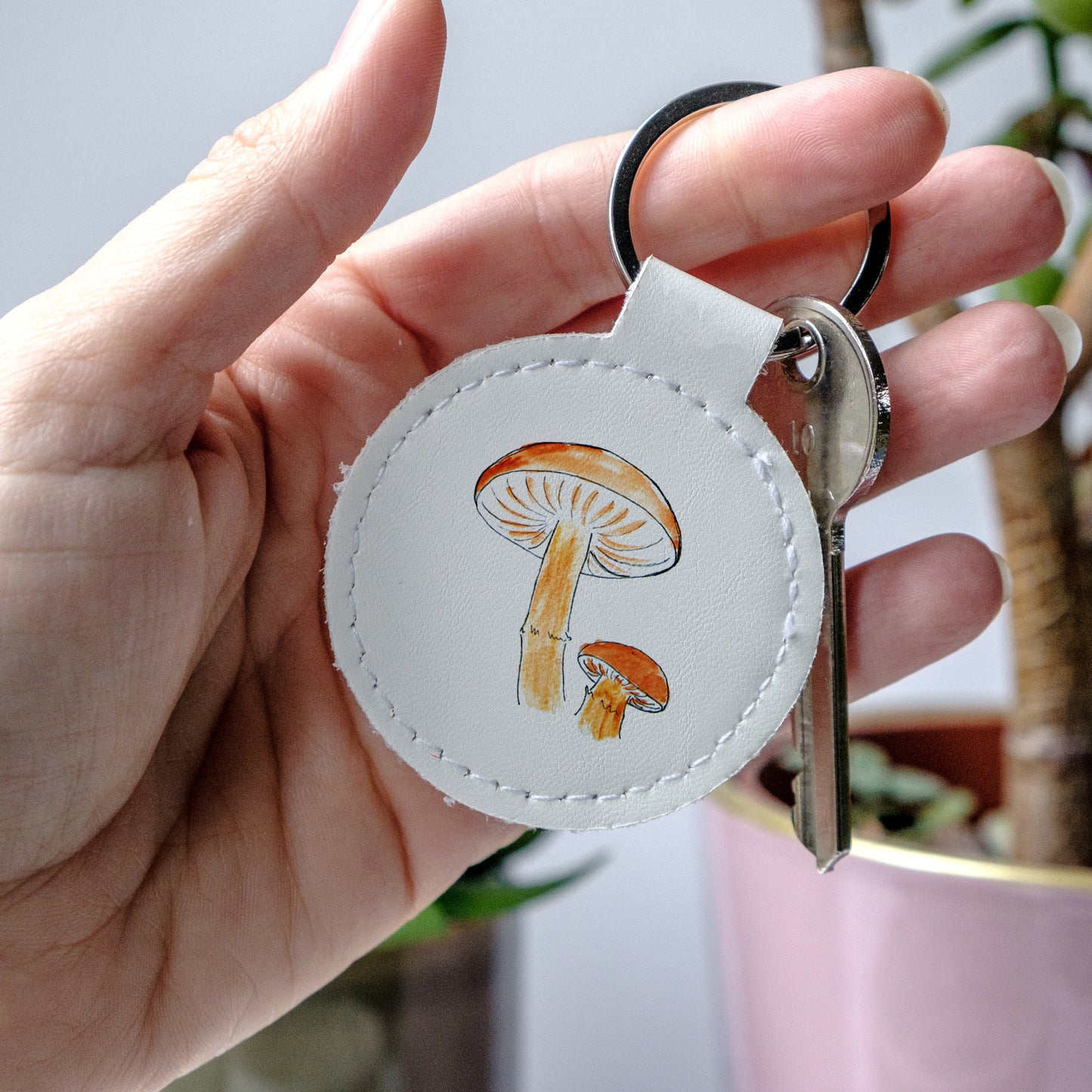 White round keychain with mushroom design held by a hand