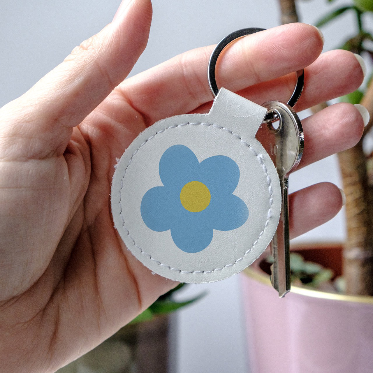 Keychain with a blue flower design held by a hand, made from high-quality faux leather and scratch-resistant print.