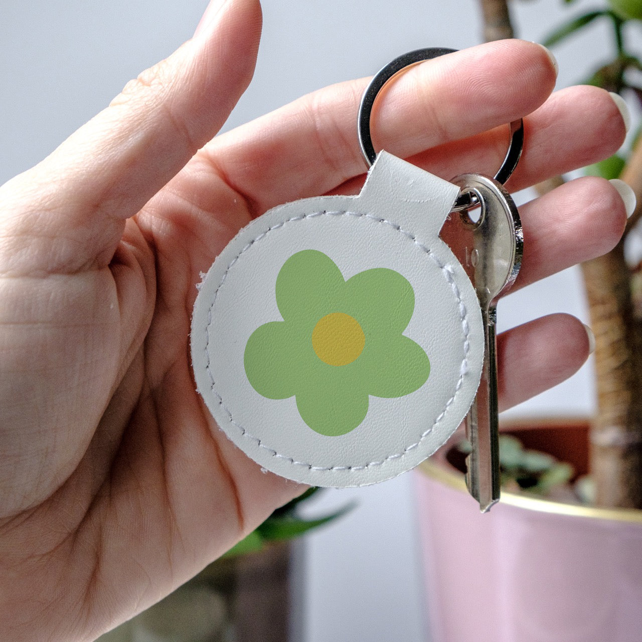 Keychain with a green flower design held by a hand, made from high-quality faux leather and scratch-resistant print.