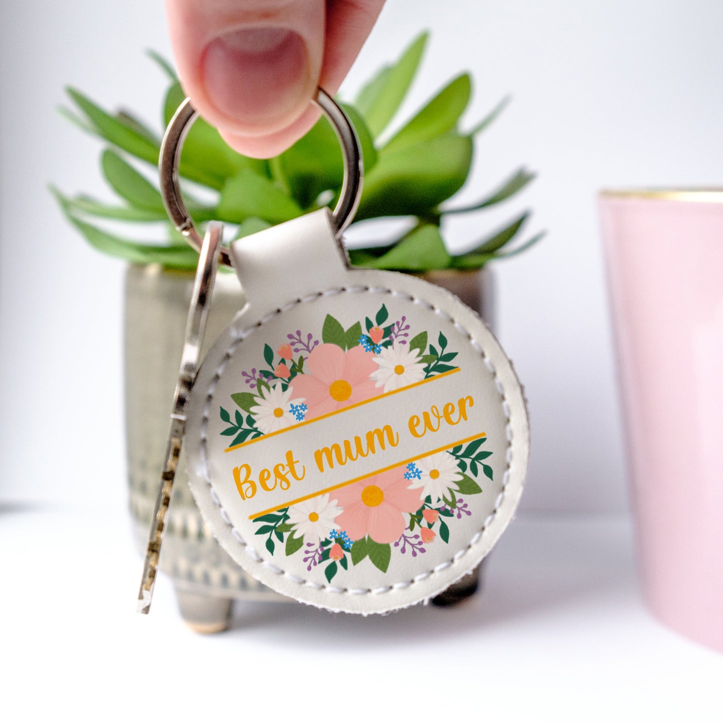 White faux leather Keychain with 'Best mum ever' text and floral design held by a hand.