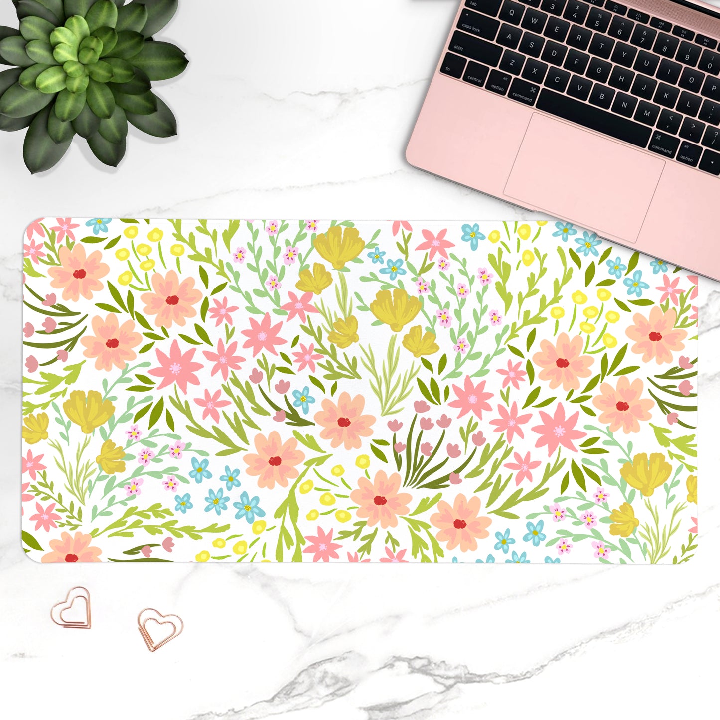 Floral desk mat with laptop, plant, and heart-shaped objects on a marble surface