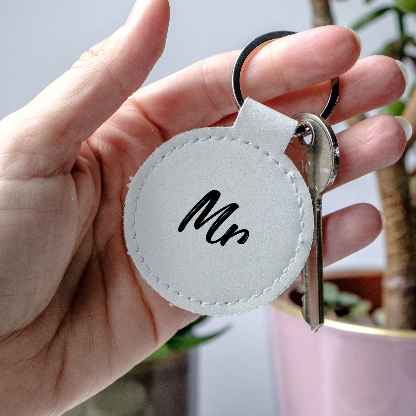 Hand holding a white leather keychain with black writing 'Mr'