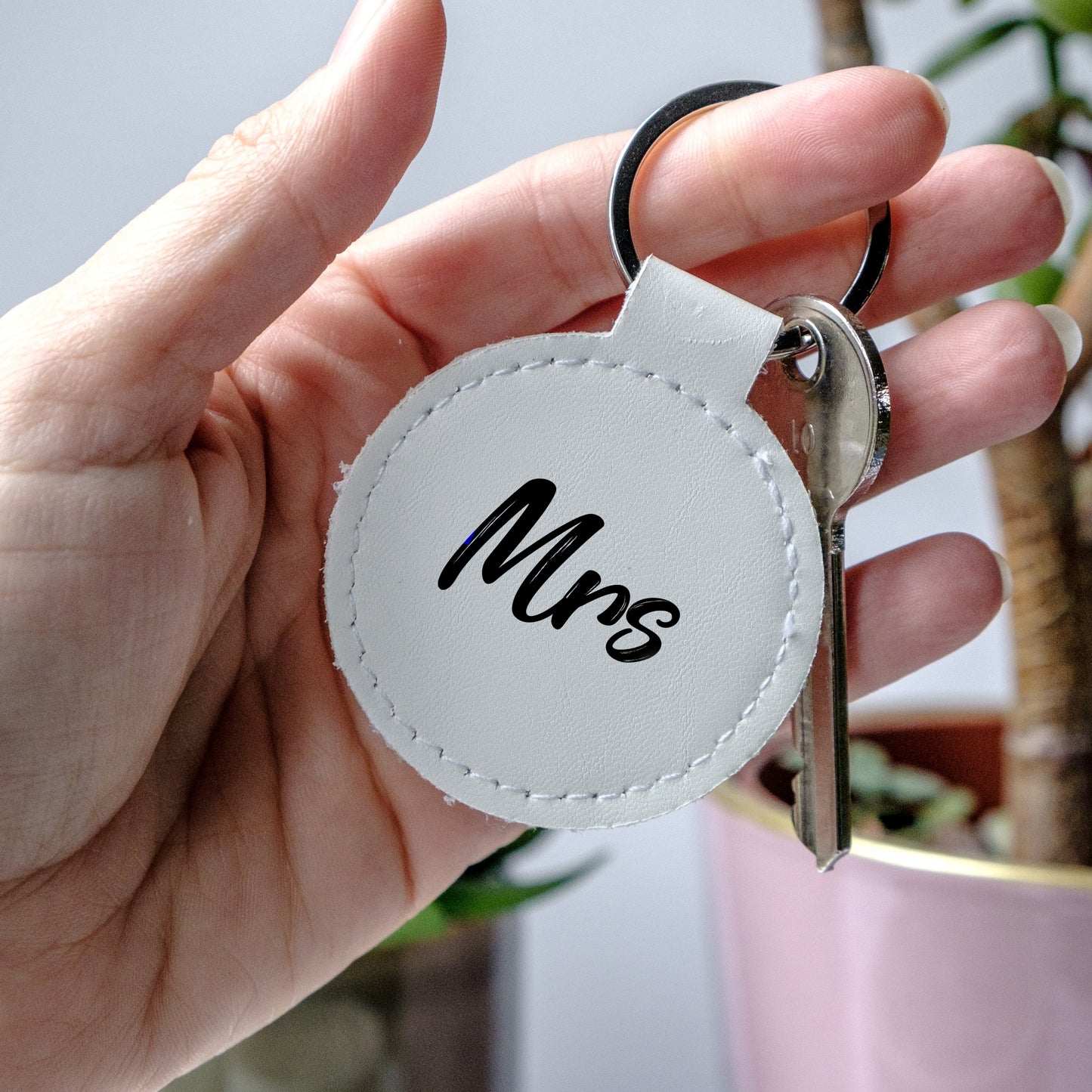 Hand holding a white leather keychain with black writing 'Mrs'