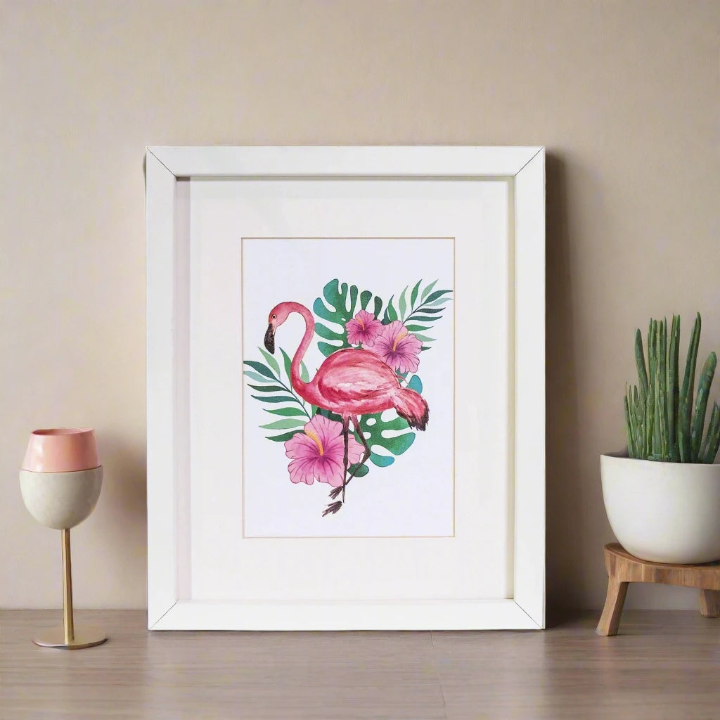 Framed artwork of a pink flamingo with flowers and leaves on a table with a plant and decorative glass ball in the background.