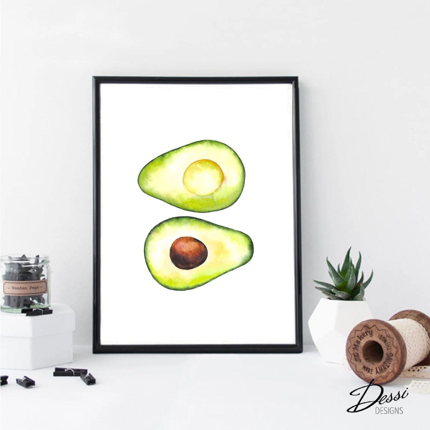 Framed artwork of a halved avocado on a white wall with decorative items below.