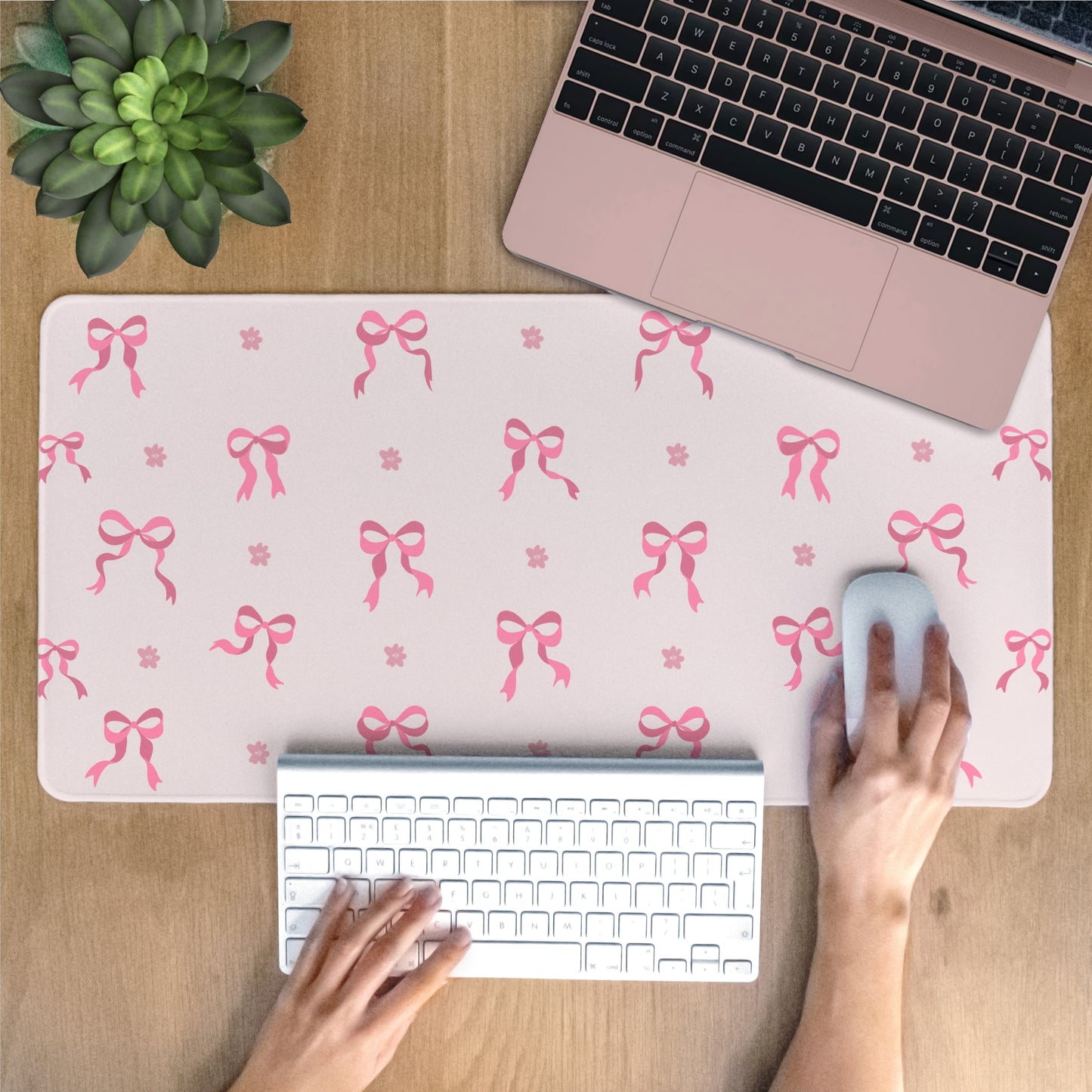 Person using a laptop with a pink bow patterned desk mat on a wooden desk.