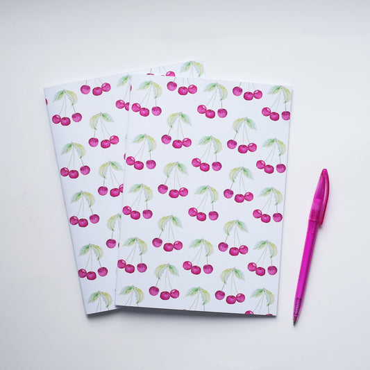 Two notebooks with cherry pattern and a pink pen on a white background