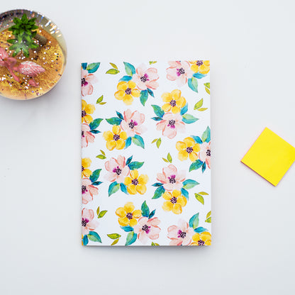Floral-patterned notebook on a light gray surface with a yellow sticky note and decorative snow globe