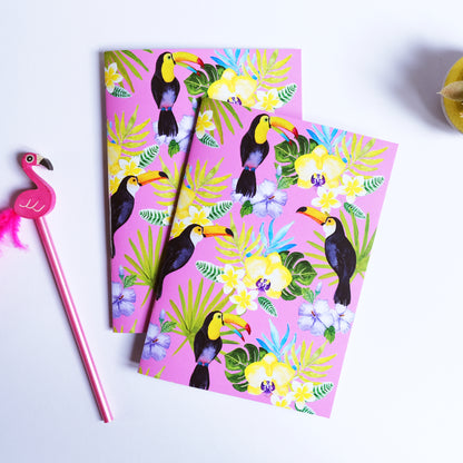 Two notebooks with a tropical bird design on a pink background, accompanied by a pink flamingo pen.