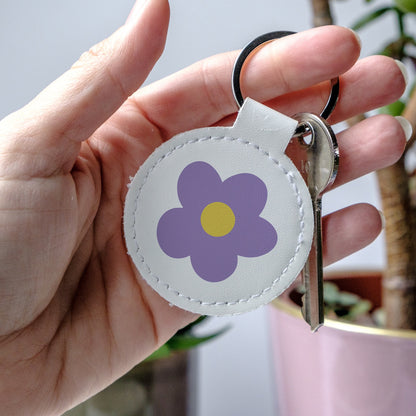 Keychain with a Purple flower design held by a hand, made from high-quality faux leather and scratch-resistant print.