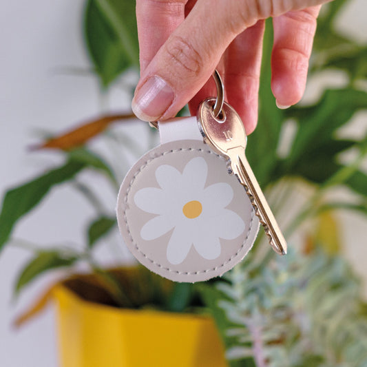 Round leather Keychain with daisy design on a beige background, held by a hand, perfect for keeping keys organised.