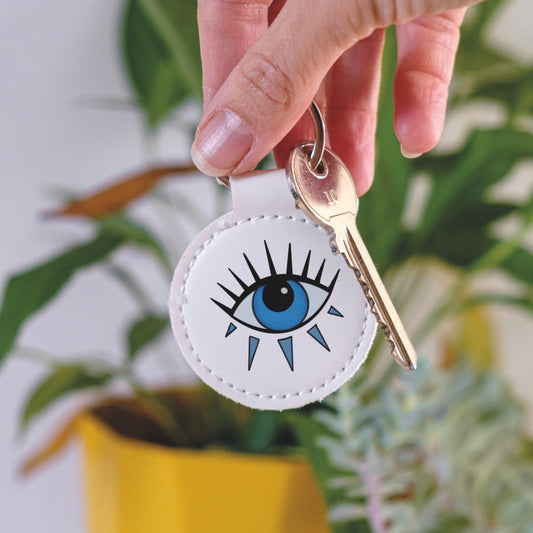 White Leather Keychain with evil eye design held by a hand in front of a plant