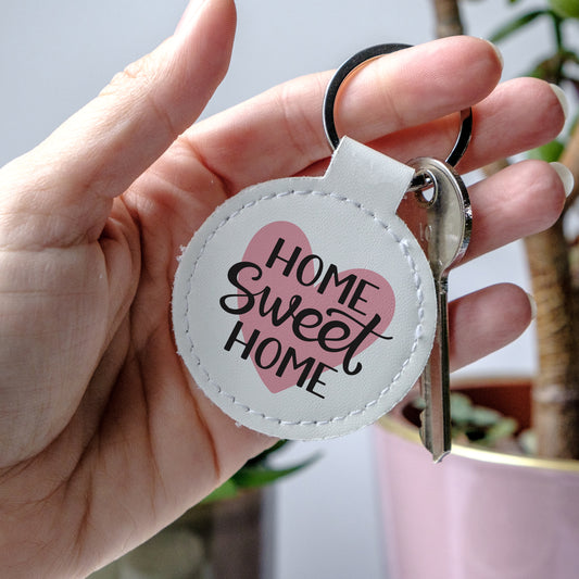 Round leather Keychain with 'Home Sweet Home' text over a pink heart, held by a hand - perfect little gift for new homeowners