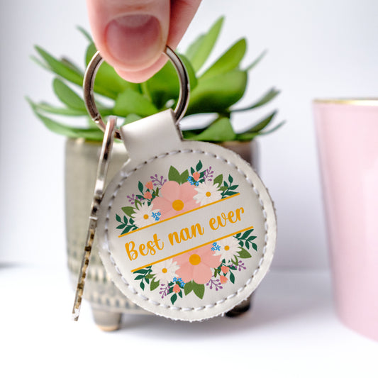 White faux leather Keychain with 'Best nan ever' text and floral design held by a hand.