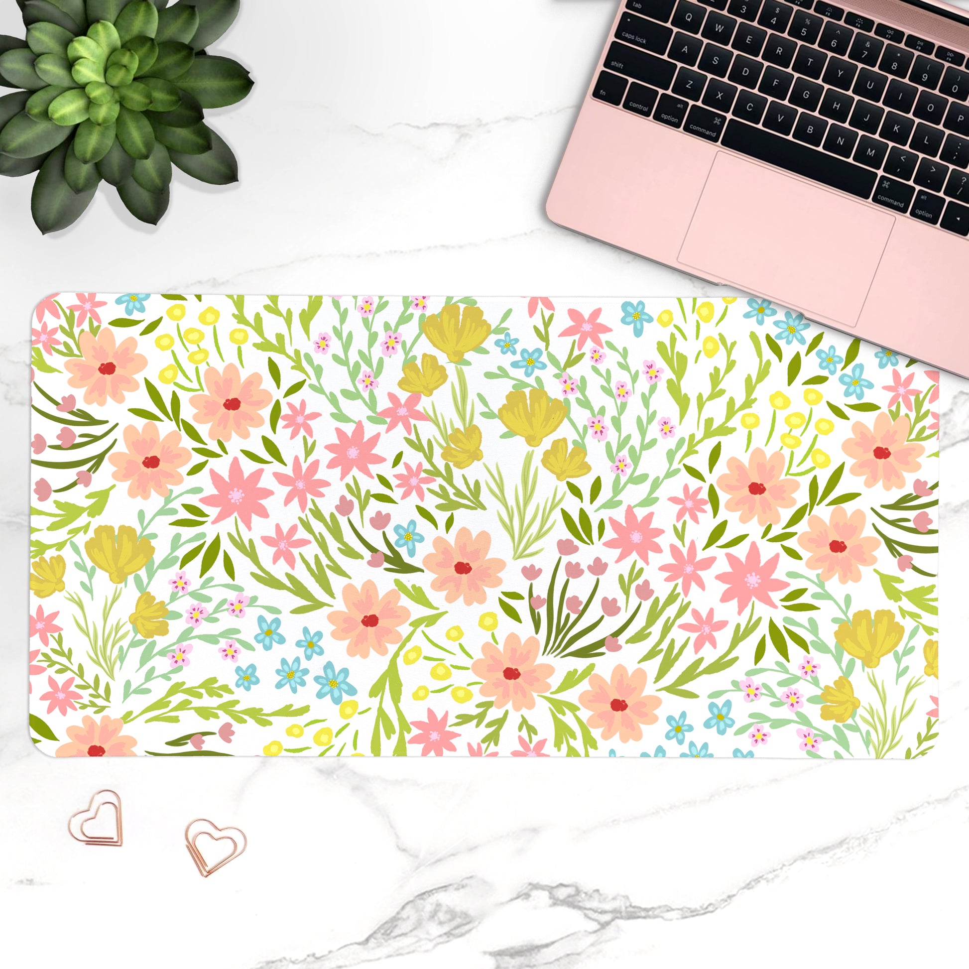 Floral desk mat with laptop, plant, and heart-shaped objects on a marble surface
