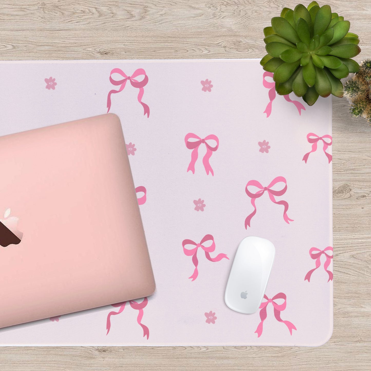Pink laptop and white mouse on a desk with a decorative pink bow patterned desk mat.