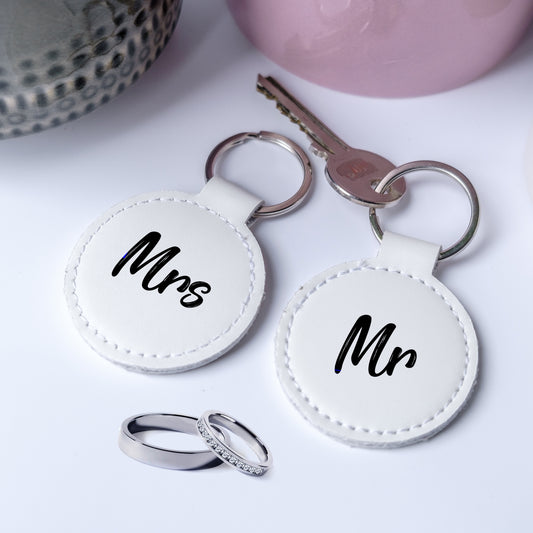 A set of Two white faux leather keychains labeled “Mr” and “Mrs” with rings and a key on a light background — perfect for newlyweds