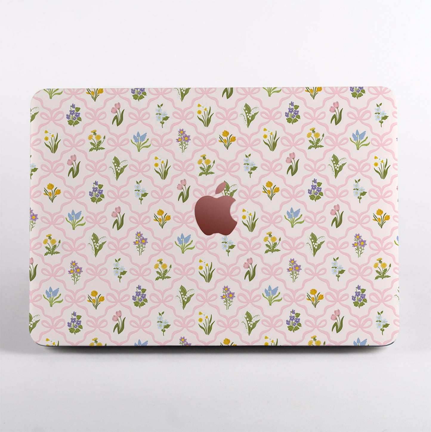 MacBook case featuring a vintage wildflower and pink bow pattern, with a cut-out Apple logo surrounded by spring floral illustrations.
