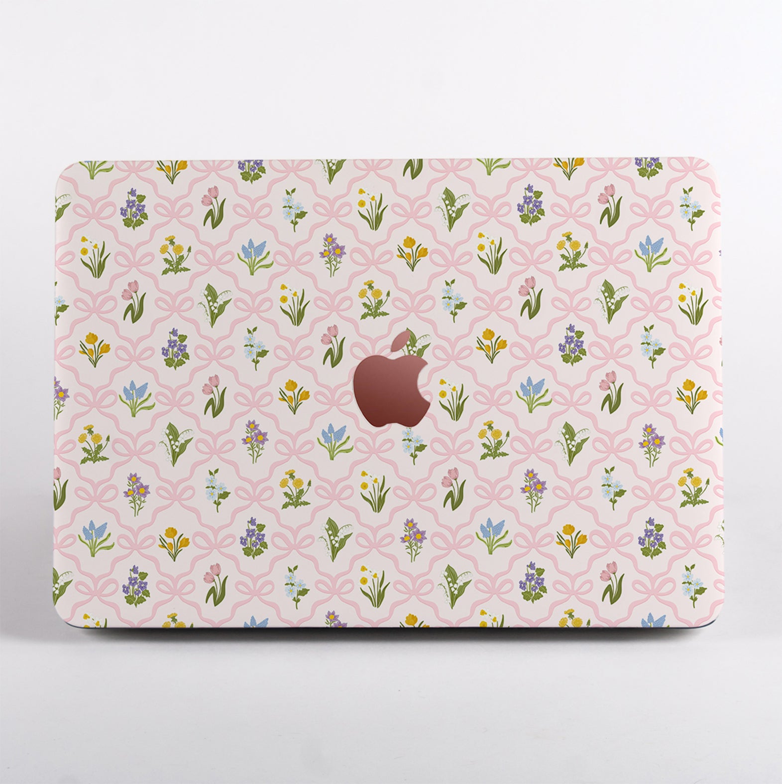 MacBook case featuring a vintage wildflower and pink bow pattern, with a cut-out Apple logo surrounded by spring floral illustrations.