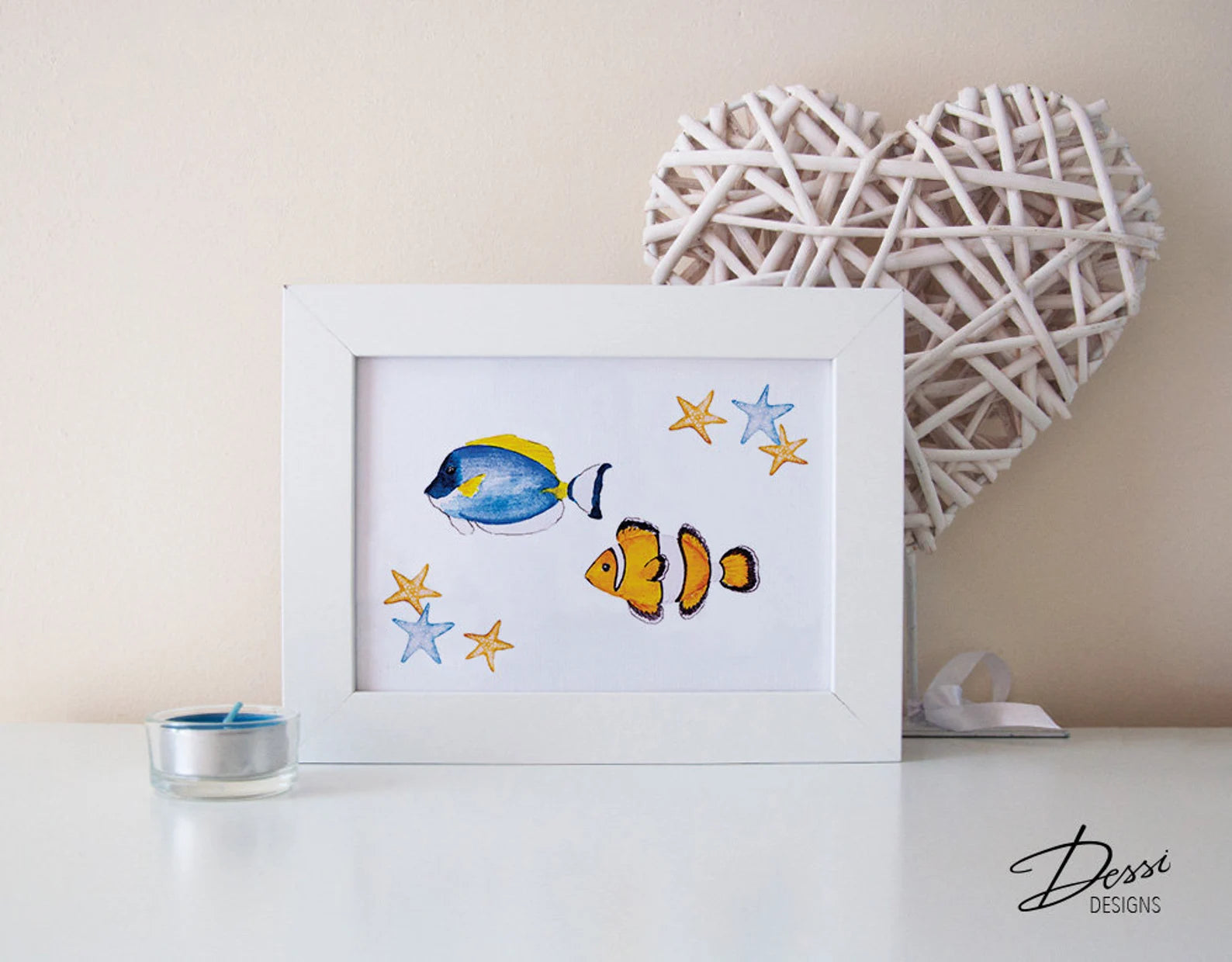 Framed artwork of two fish and stars on a white surface with a decorative heart and candle in the background.