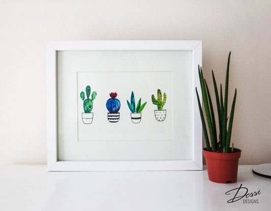 Framed artwork of cacti on a white surface with a plant in the background