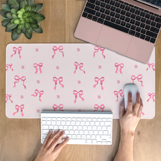 Person using a laptop with a pink bow patterned desk mat on a wooden desk.