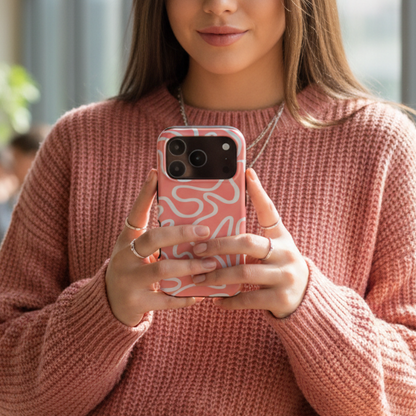 Woman in a pink sweater holding a phone with a tough pink case featuring white abstract line art — a stylish, durable design for extra protection